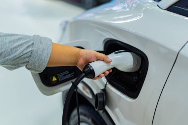 Bir kişi elektrikli araba şarj aleti tutuyor ve elektrikli araba aküsünü şarj ediyor..