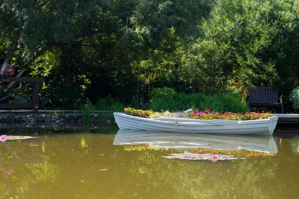 Park'ta gölde serbestçe yüzen beyaz bir teknede çiçekler, çiçek yatağı yerine bir tekne, peyzaj