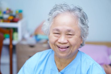 Asya kıdemli veya yaşlı yaşlı kadın kadın hasta hastane koğuşunda hemşirelik yatakta otururken parlak face smile: sağlıklı güçlü tıp kavramı 