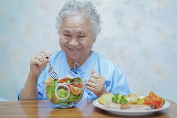 Asian senior or elderly old lady woman patient eating breakfast healthy food with hope and happy while sitting and hungry on bed in hospital.