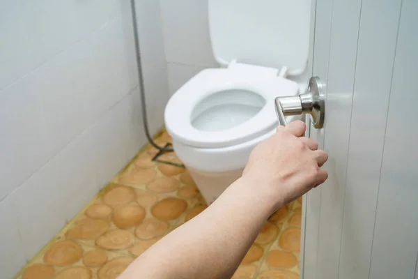 Asian middle-aged lady woman patient open toilet by her hand in hospital.