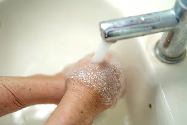 Asian senior elderly old lady woman patient washing hands in toilet bathroom the hospital ward : healthy medical concept