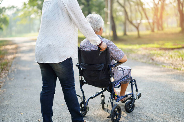 Asian senior or elderly old lady woman patient with care, help and support on wheelchair in park in holiday: healthy strong medical concept.