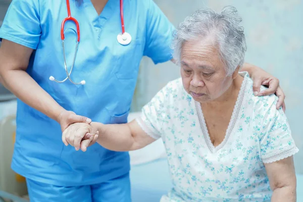 Asian nurse physiotherapist doctor care, help and support senior or elderly old lady woman patient lie down in bed at hospital ward : healthy strong medical concept.