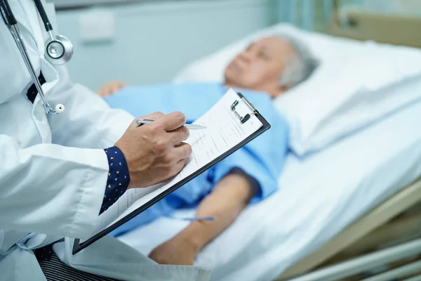 Doctor writing down the diagnosis on clipboard while Asian senior or elderly old lady woman  lying on bed in nursing hospital ward : healthy strong medical concept
