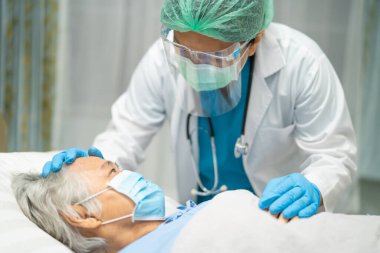 Karantina hemşirelik koğuşundaki Covid-19 Coronavirus salgınını koruyan yaşlı kadın hastaları kontrol etmek için yüz maskesi ve PPE kıyafeti giyen Asyalı doktor..