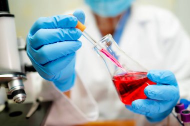 Bilimsel kimya laboratuvarında kırmızı renkli sıvı çözeltisi olan konik cam şişeyi elinde tutan bilim adamı..