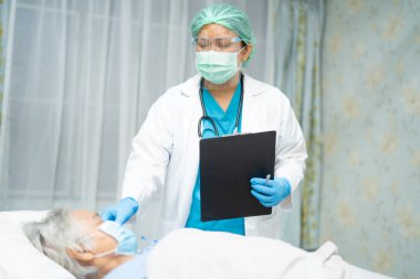 Doktor, enfeksiyonu korumak ve Novel Coronavirus Covid-19 virüsünü öldürmek için hastanede yüz maskesi takan Asyalı yaşlı ya da yaşlı kadın hastaları kontrol etmek için stetoskop kullanıyor..