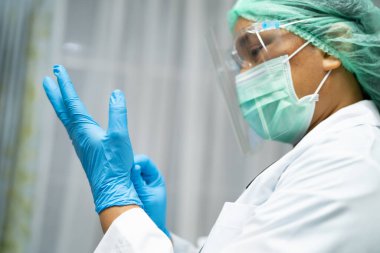 Karantina hemşirelik koğuşunda Covid-19 Coronavirus salgınını kontrol etmek için yüz maskesi takan Asyalı doktor, PPE giysisi ve küre..