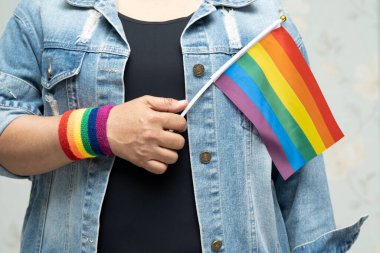 Mavi kot ceket ya da kot pantolon giyen ve elinde gökkuşağı renkli bayrak tutan Asyalı kadın, LGBT gurur ayının sembolü, Haziran sosyal ortamında eşcinsel, lezbiyen, biseksüel, transseksüel, insan hakları.