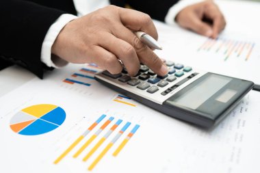 Modern ofis, finans ve iş konseptinde grafik grafik grafiği ve hesap makinesiyle çalışan ve finansal raporları analiz eden Asyalı muhasebeci.