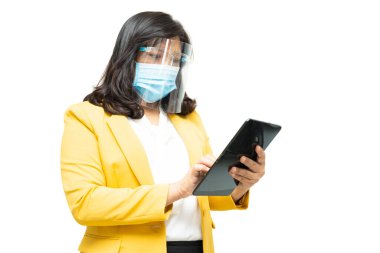 Asyalı iş kadınları beyaz arka planda maske ve yüz koruması takarak tablet kullanıyor. Ofiste Covid-19 Coronavirus salgınını korumak için yeni bir normal..