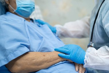 Doktor, enfeksiyon kapmasın diye hastanede yüz maskesi takan Asyalı yaşlı ya da yaşlı kadın hastaları kontrol etmek için steteskop kullanıyor..