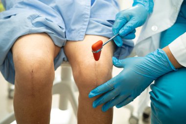 Ortopedi kliniğinde kıdemli bir hastanın diz ve bacağını muayene eden Asyalı doktor fizyoterapisti..