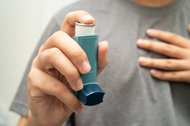 Astım ve kronik obstrüktif akciğer hastalığı COPD, Asyalı genç adam ölçülü doz solunum cihazı kullanıyor..
