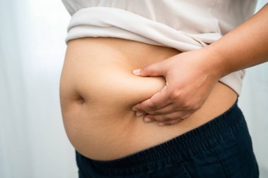 Asyalı kadın şişman göbeğini sıkmak için elini kullanıyor. Büyük boy aşırı kilolu ve obez..