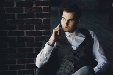 Yakışıklı işadamı sandalyede oturan ve pencereden seyir sırasında cep telefonundan konuşuyor.