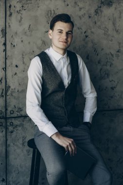 Çekici bir adam gri bir arka plan üzerinde bir sandalyede oturan bir takım elbise giymiş.