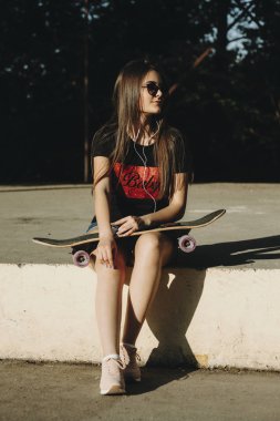 Bir kaykay üzerinde bacaklarını uzakta müzik dinleme seyir ile bir skatepark oturan çekici beyaz uzun saçlı kız .