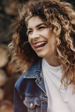 Denim ceket giymiş kıvırcık kadın inanılmaz gülüyor ve uzağa arıyorsunuz.