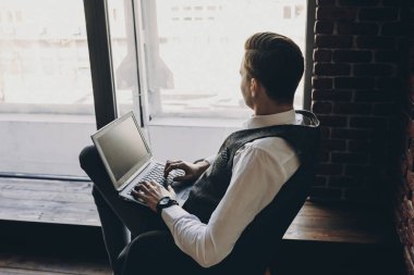 Kness uzakta pencereden görünümlü yakışıklı dalgın biri dizüstü bilgisayar ile yan görünüm.