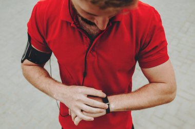 Kırmızı bir gömlek giymiş genç sporcu saatine bakıyor ve çalıştırmak hazırlanıyor.