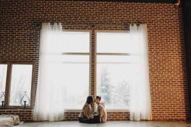 Yüz yüze ve büyük bir pencere karşı öpüşme katta oturan hoş bir çift tam uzunlukta portresi.