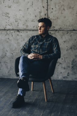 Bir sandalyede oturuyor ve uzak ciddi görünümlü gri bir duvara güzel genç adam.