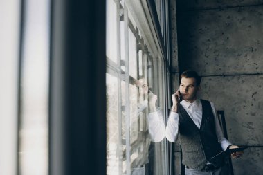 Bir pencere kalmak ve el dijital tablet ile telefonda konuşurken yakışıklı işadamı.