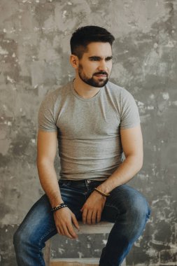 O n sandalye oturma ve uzak gri bir duvara bakarak yakışıklı sakallı adam portresi.