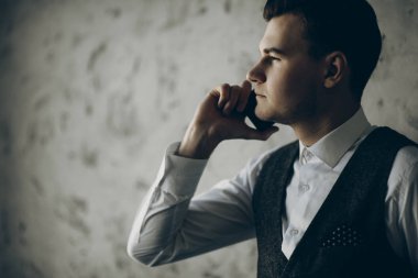 Gri bir arka plan telefonda konuşurken bir işadamı yan görünüm.