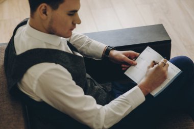 Genç adam kanepede oturan ve planlarını bir Not Defteri'nde yazma. 