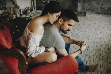 Çok güzel çift Vintage kırmızı sandalyede oturan kırmızı dudaklı kız dan kucaklayan dövme nerede geri hafifçe başını ona dönüyor iken onun boynunu öpmeye bekleyen sevgilisi.