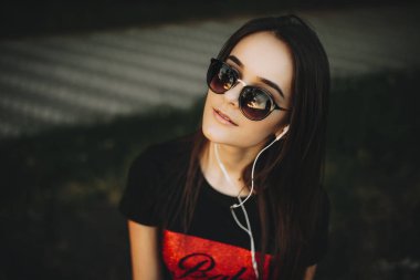 Güneş gözlüğü ve kameraya bakarak earphones ile güzel bir genç kız portresi kapatın.