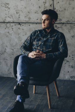 Güzel genç adam sandalyede rahat oturuyor ve uzağa arıyorsunuz.