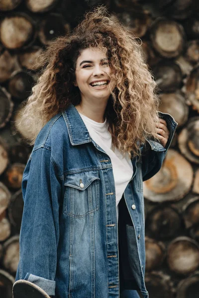 Beautiful curly young woman laughing and looking into camera while playing with hand in her hair.