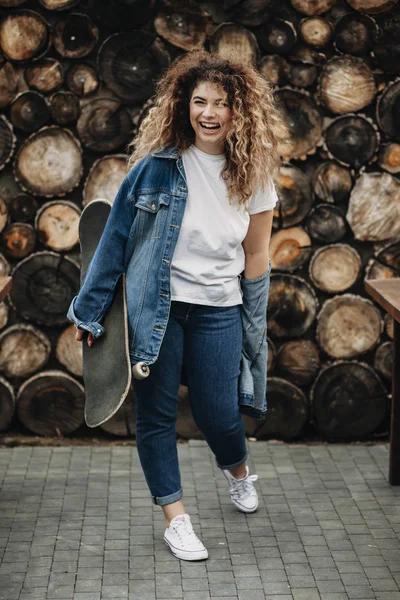 Lycklig Kvinna Med Skateboard Hand Klädd Vardagligen Skrattar Och Tittar — Stockfoto