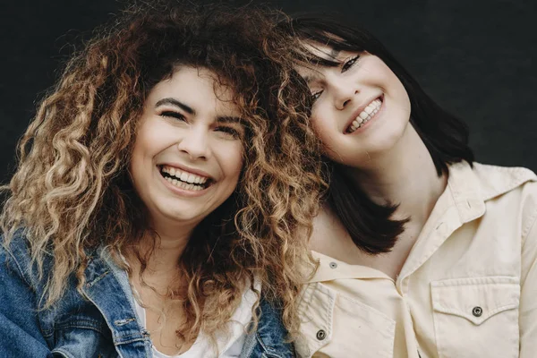 Close up portrait of a denim young women laughing and looking into camera against a black wall.