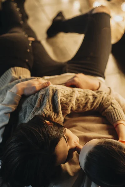 Upper view of a amazing caucasian couple leaning on the floor and kissing near a warm light in a dark room.