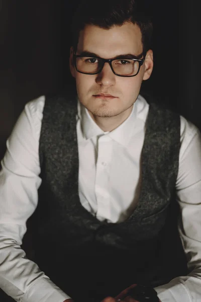 Portrait of handsome young executive with glasses sitting on a chair and watching into the camera.