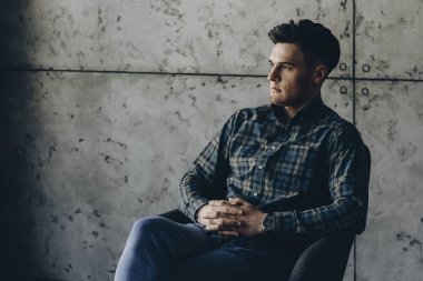 Sandalyede oturan ve pencereden bakarak çekici genç adam portresi.