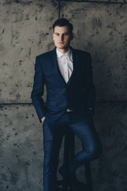 Gri bir arka plan üzerinde kalan bir takım elbise giymiş çekici bir adam portresi.