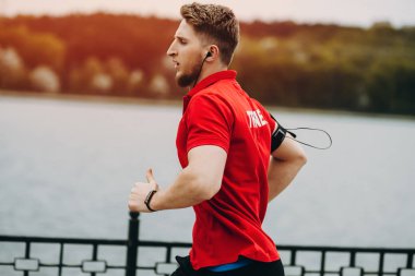 Çekici kaslı adam güzel bir parkta ellerde gadget'lar ile koşuyor.