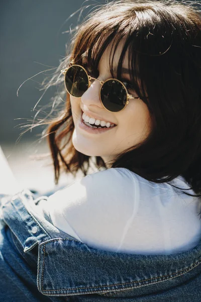 Lovely close up portrait of young caucasian brunette with sunglasses and short hair looking into camera laughing.