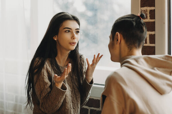 Young brunette girl talking and explaining something to her boyfriend in a warm room.