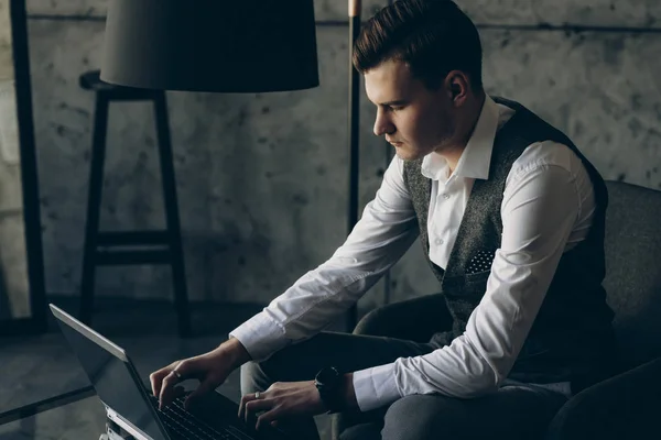 Handsome young executive working at laptop in the office sitting in a chair.