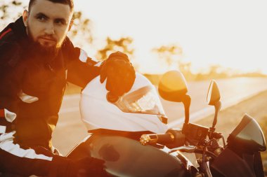 Tatil zamanlarında onun bisiklet ile yeni yerler keşfetmek emin beyaz adam. Uzak yardım günbatımı karşı onun kask üzerinde bakarken bisikletiyle oturan genç erkek.