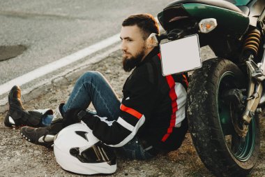 Zemin motosikletine yaslanmış ve uzağa seyahat onun zamanında dinlenme süre seyir üzerinde oturan güzel genç adam.