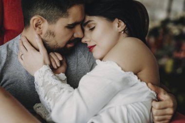 Güzel bir çift adam aşkını kırmızı bir sandalyede gülümseyen kapalı gözlerle kollarını tutuyor ise yüz yüze oturma portre kadar kapatın.