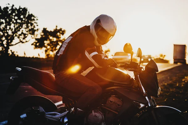 Amazing portrait of a caucasian bike adventurer sitting on his motorcycle and looking into camera with helmet on his head against beautiful sunset.